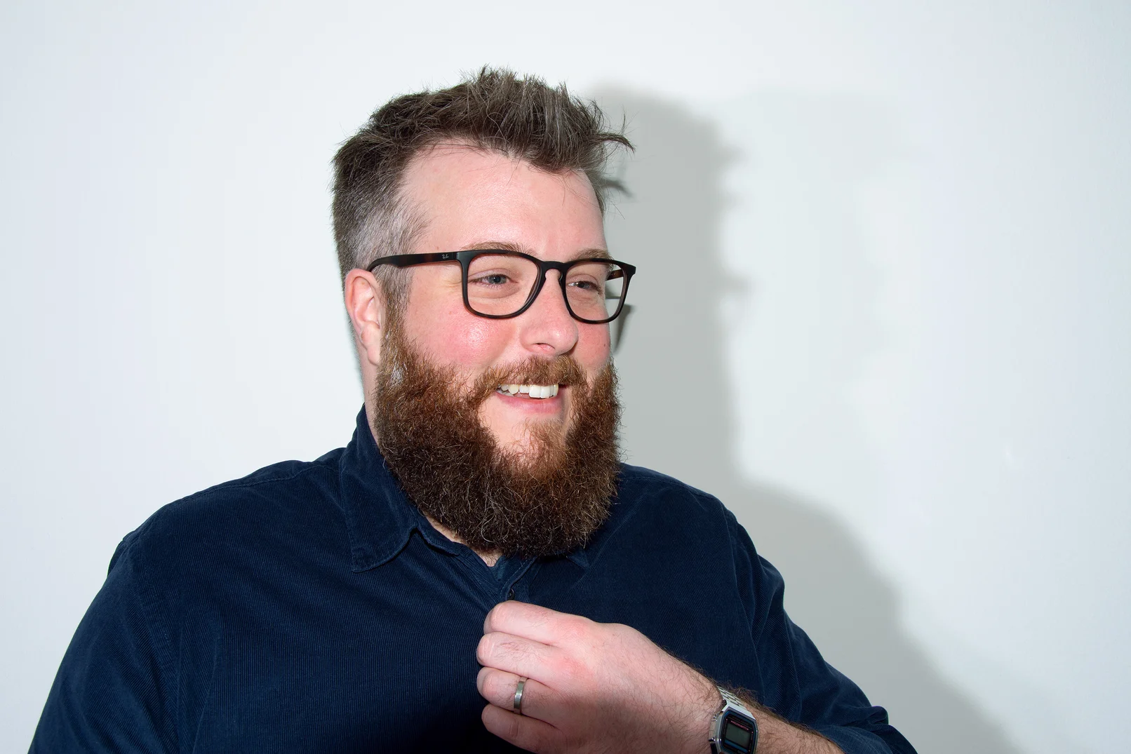 Mann vor weißem Hintergrund, der lachend an der Kamera vorbei schaut