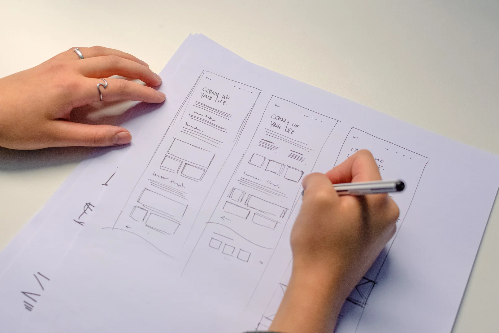 Hände die verschiedene Layoutideen auf Papier skizzieren