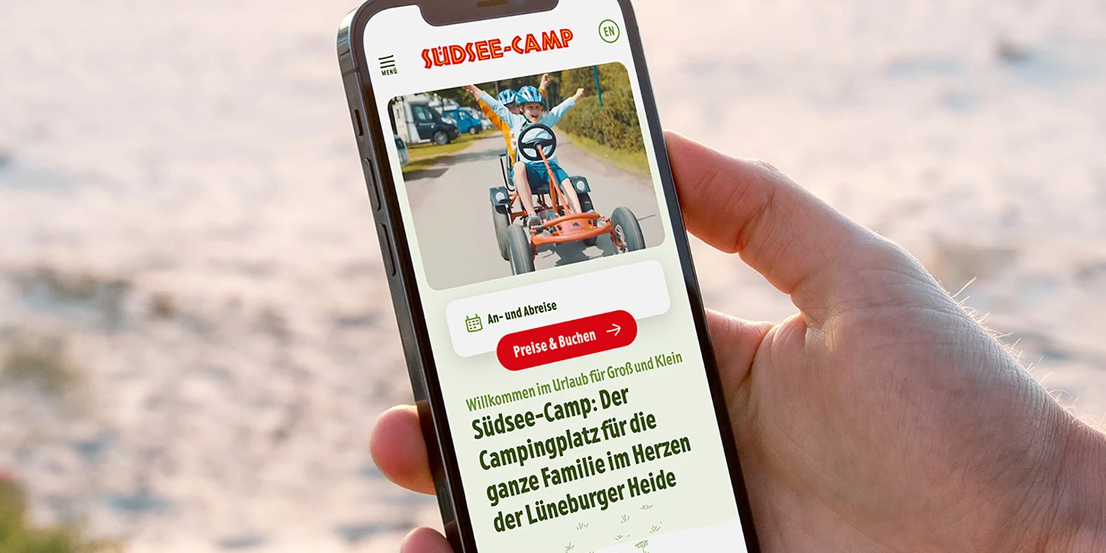Eine Hand hält ein Smartphone, auf dem die Website des Südseecamps geöffnet ist